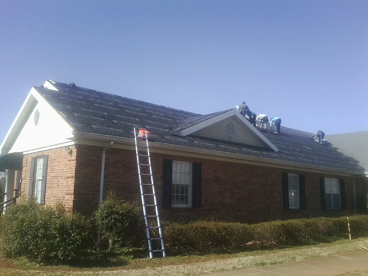 Crew tearing shingles off a brick ranch roof with a ladder set — Metal Roof Repair work by our crew in Gotha