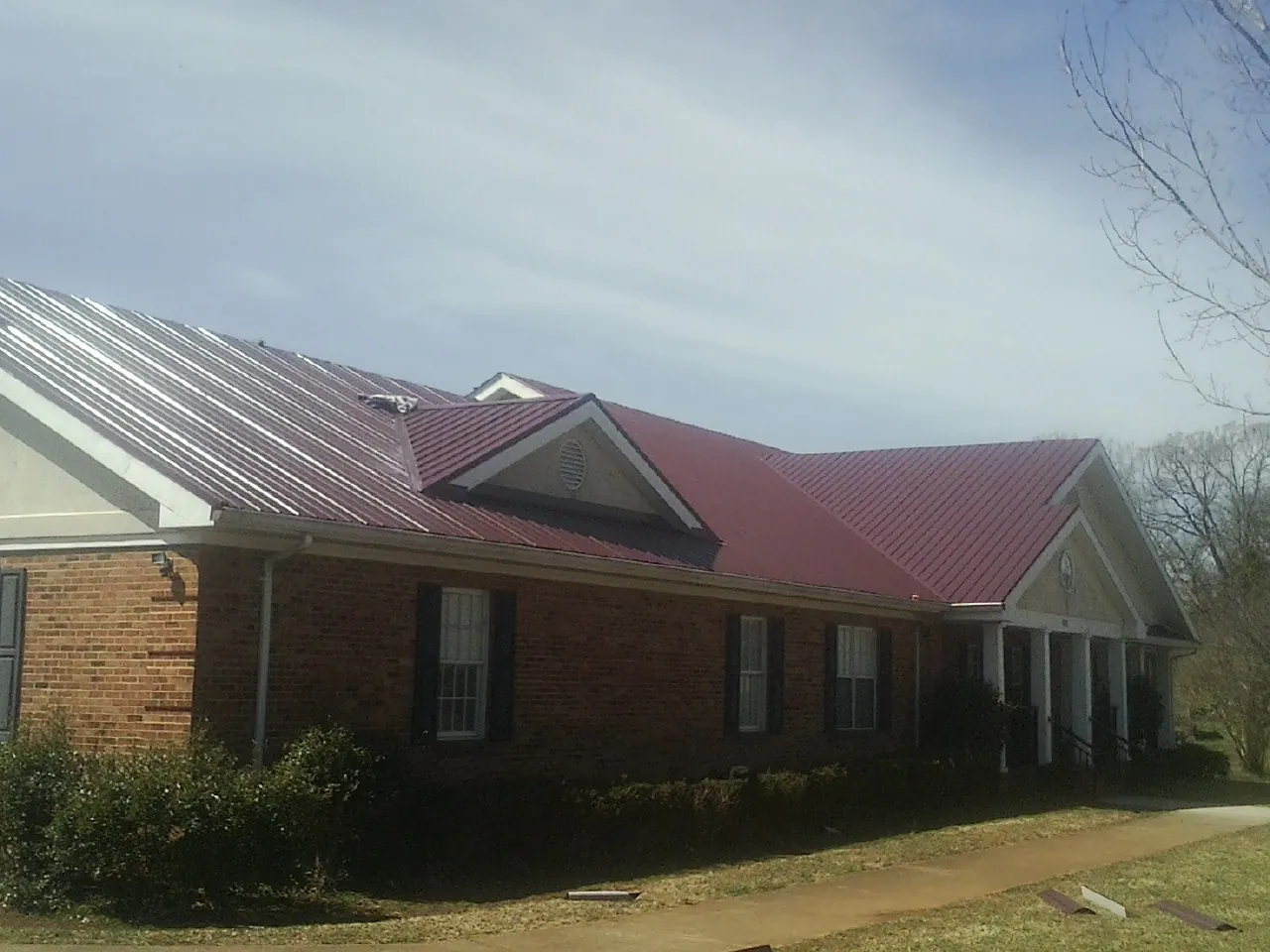 Red metal roof with gabled entries on a long brick building, from a Hail Damage Roof Repair job in Gotha