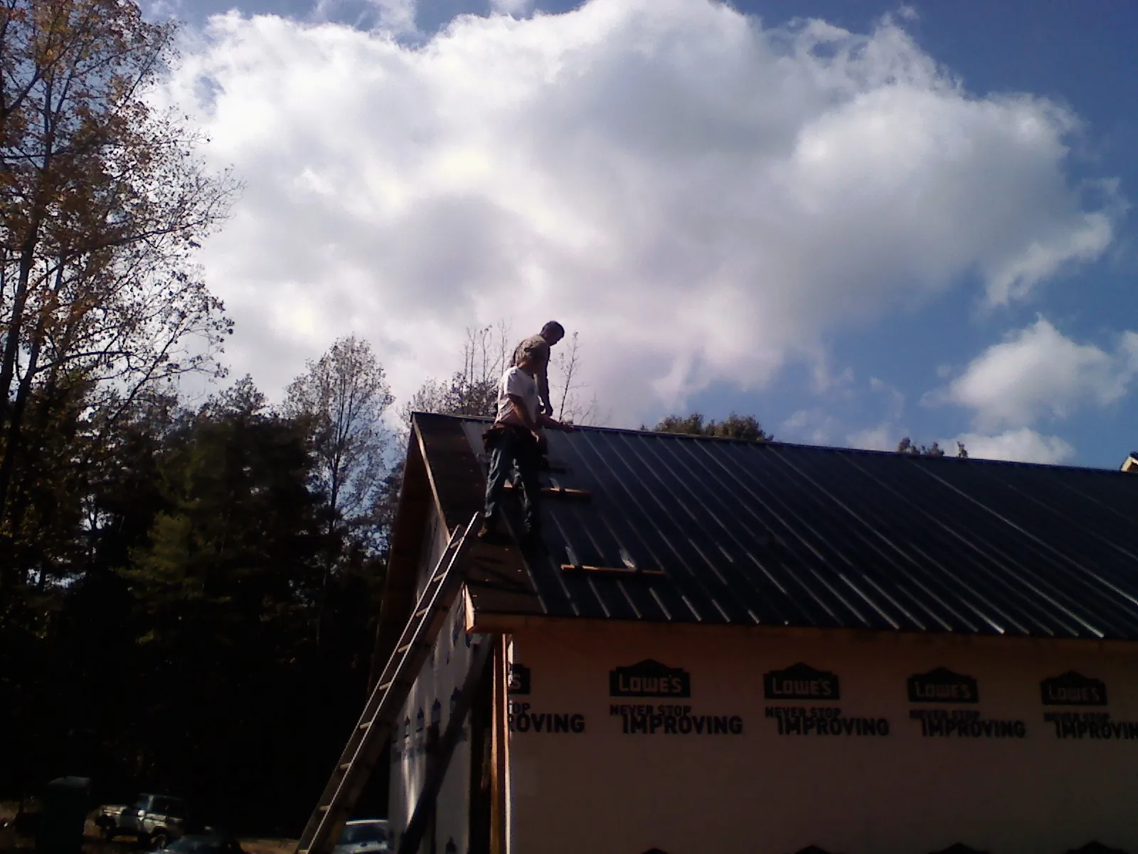 Roofer fastening dark metal panels high against a cloudy sky, from a Roof Inspection job in Gotha
