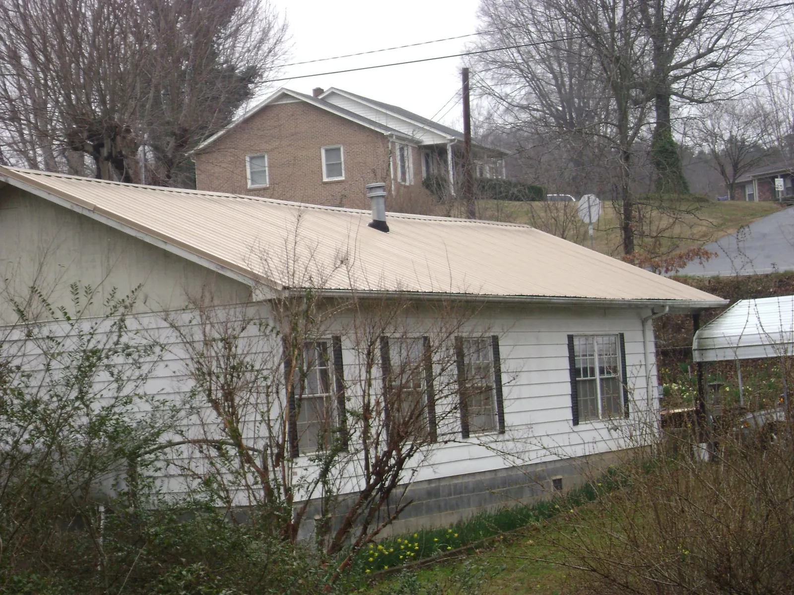 Tan metal roof on a white sided house set into a hillside — Commercial Roofing by Roofing Brothers in Gotha